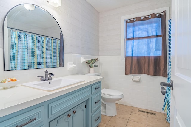 bathroom with tile patterned flooring, vanity, tile walls, toilet, and visible vents