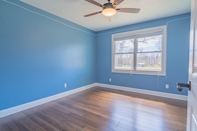 spare room with a textured ceiling, dark wood finished floors, baseboards, visible vents, and ceiling fan