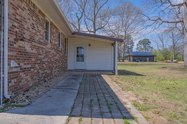doorway to property featuring a lawn and brick siding