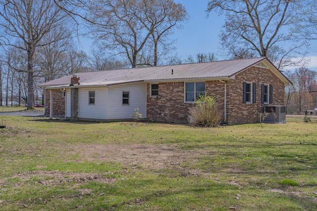 back of property with brick siding, central AC unit, a yard, and metal roof