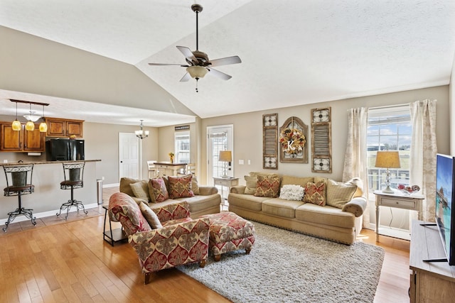 living area featuring a textured ceiling, baseboards, lofted ceiling, light wood-style floors, and ceiling fan with notable chandelier