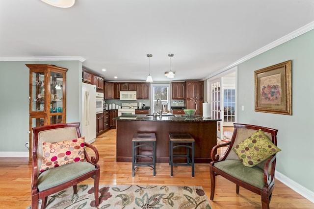 kitchen with light wood finished floors, white appliances, ornamental molding, a sink, and a kitchen breakfast bar
