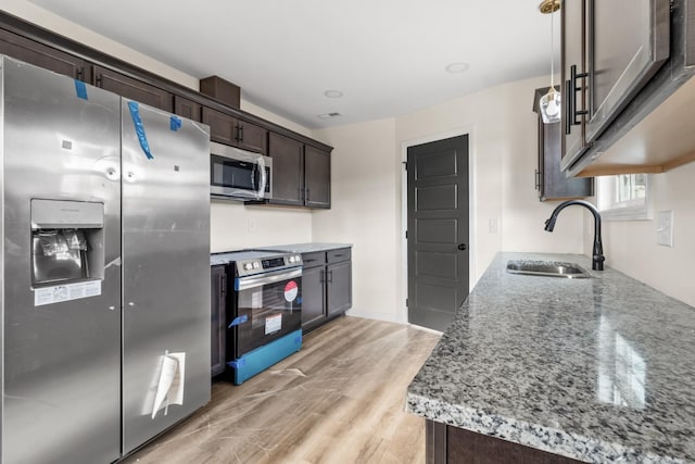 kitchen featuring light wood finished floors, light stone countertops, appliances with stainless steel finishes, dark brown cabinetry, and a sink