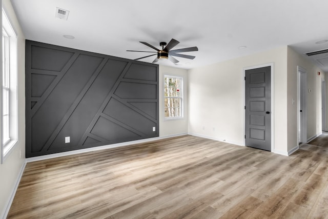 spare room with a decorative wall, baseboards, light wood-style floors, visible vents, and a ceiling fan