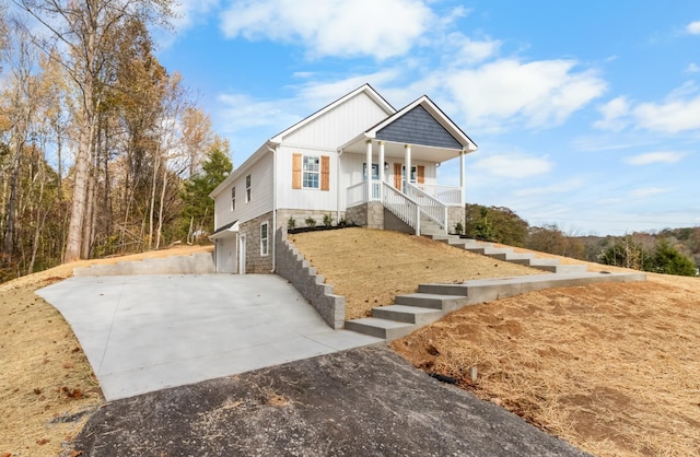 view of front of property with stairs, driveway, stone siding, and a porch
