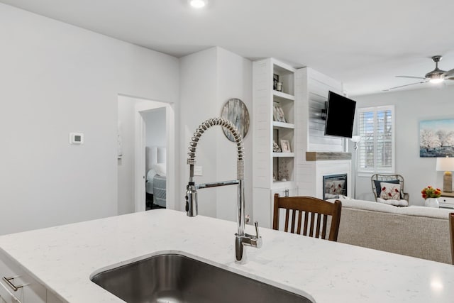 kitchen with open floor plan, a sink, ceiling fan, light stone countertops, and a fireplace