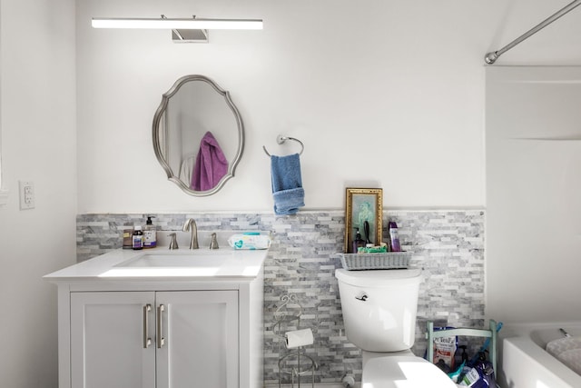 bathroom featuring a wainscoted wall, toilet, vanity, a bath, and tile walls
