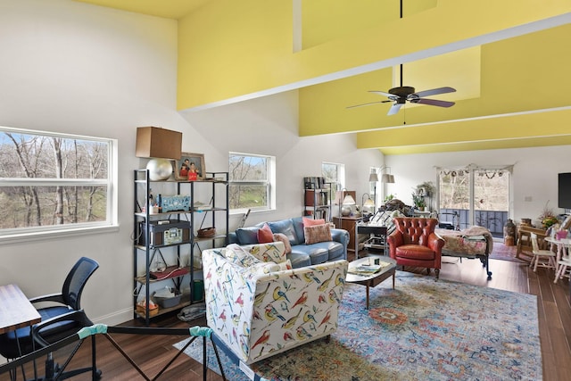 living area featuring a high ceiling, baseboards, ceiling fan, and wood finished floors