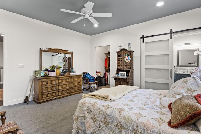 bedroom with baseboards, a ceiling fan, a barn door, carpet floors, and a walk in closet