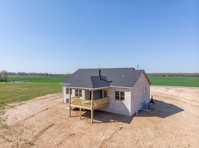 rear view of property with central AC, roof with shingles, a wooden deck, and a rural view