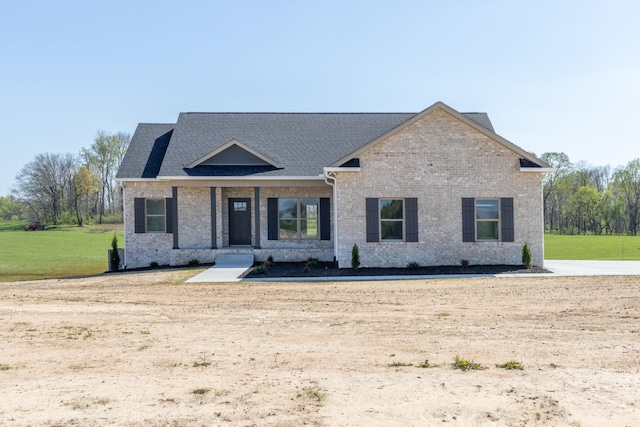 view of front of home with a front yard, brick siding, and a shingled roof