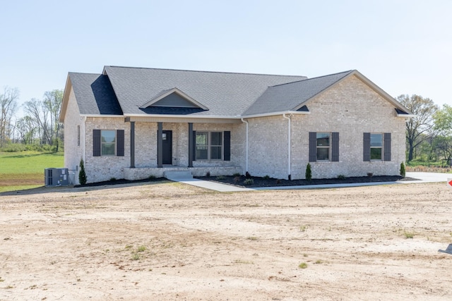 view of front of home featuring roof with shingles, brick siding, and central AC unit