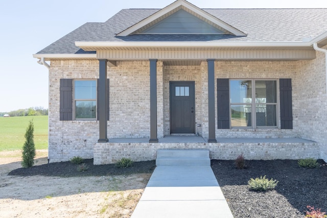 property entrance featuring brick siding, a porch, and a shingled roof
