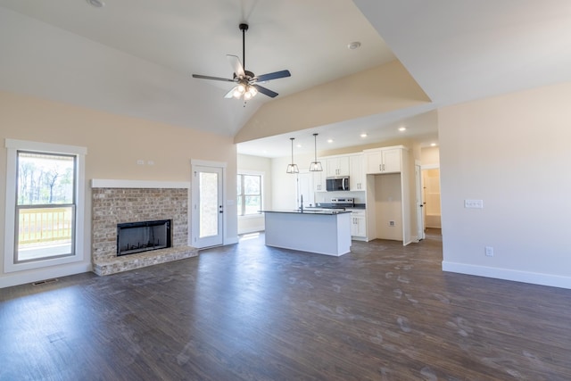 unfurnished living room featuring baseboards, a brick fireplace, dark wood-style flooring, a ceiling fan, and lofted ceiling