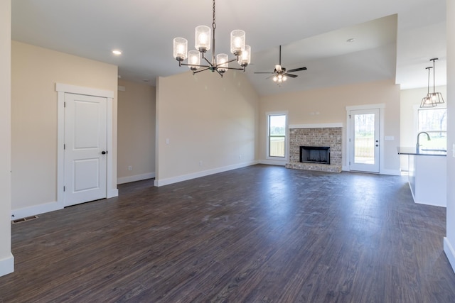 unfurnished living room with ceiling fan with notable chandelier, baseboards, dark wood finished floors, and visible vents