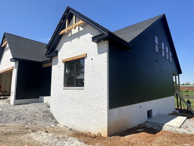 view of side of home with a shingled roof and brick siding
