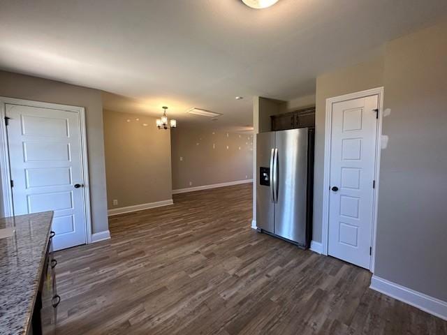 kitchen with a chandelier, light stone countertops, stainless steel fridge, baseboards, and dark wood-style flooring