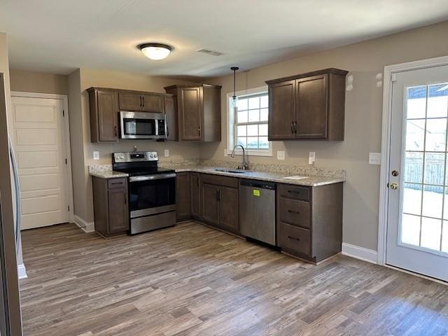 kitchen with stainless steel appliances, baseboards, a sink, light wood-style flooring, and dark brown cabinetry