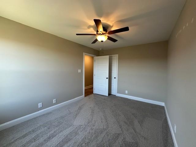 unfurnished room with dark colored carpet, baseboards, and ceiling fan
