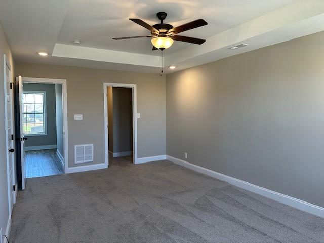 empty room with a ceiling fan, a raised ceiling, baseboards, visible vents, and carpet