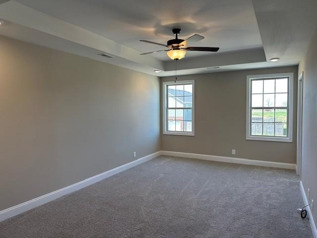 empty room featuring a tray ceiling, baseboards, visible vents, ceiling fan, and carpet