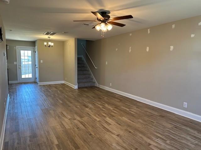 unfurnished living room with dark wood-style flooring, visible vents, baseboards, stairway, and ceiling fan with notable chandelier