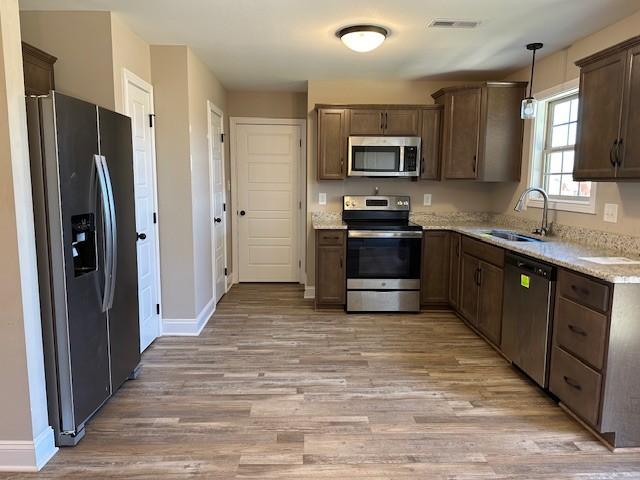 kitchen featuring light wood-type flooring, stainless steel appliances, baseboards, a sink, and pendant lighting