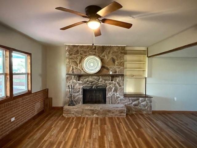 unfurnished living room with baseboards, ceiling fan, a stone fireplace, and wood finished floors