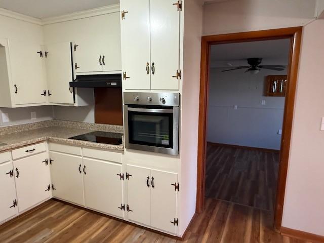kitchen featuring wood finished floors, under cabinet range hood, black electric stovetop, and oven