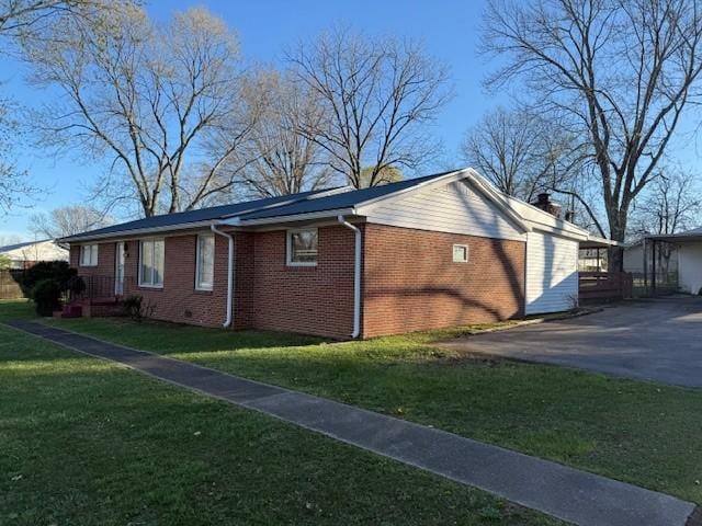 view of side of property featuring a lawn, driveway, and brick siding