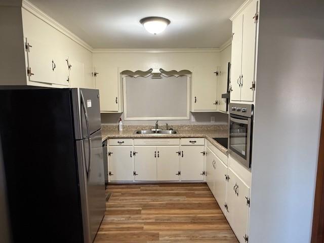kitchen with a sink, white cabinets, light wood-style floors, ornamental molding, and stainless steel appliances