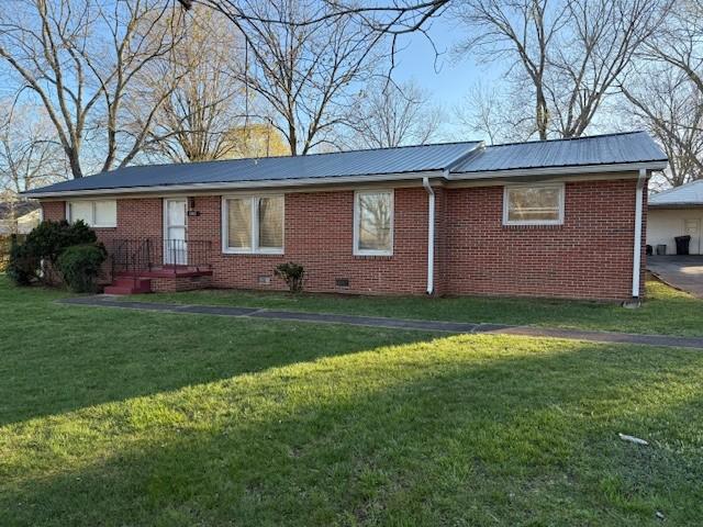 view of front of property featuring brick siding, a front lawn, crawl space, and metal roof