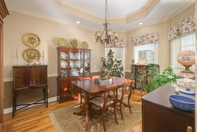 dining space featuring an inviting chandelier, light wood-style floors, crown molding, and a raised ceiling