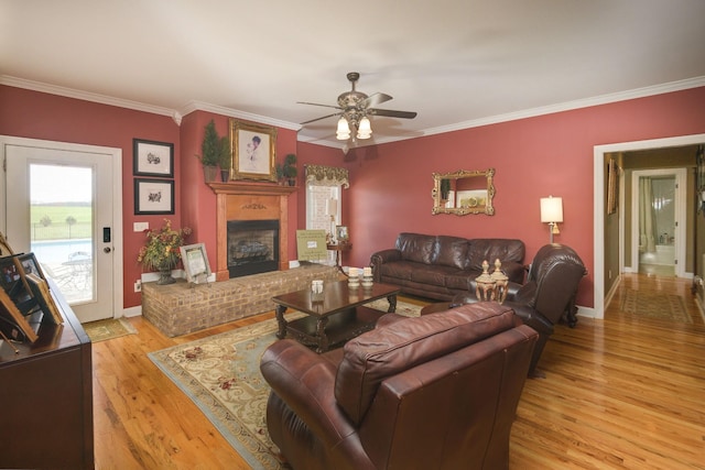 living room with crown molding, a brick fireplace, baseboards, a ceiling fan, and light wood-type flooring
