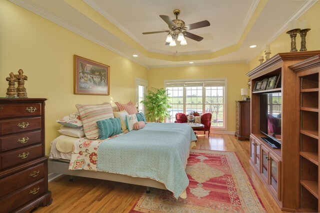 bedroom with a ceiling fan, a raised ceiling, crown molding, and light wood-style floors