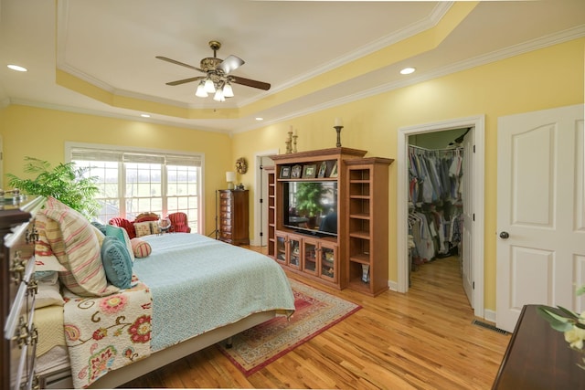 bedroom with a tray ceiling, crown molding, light wood-type flooring, a spacious closet, and visible vents