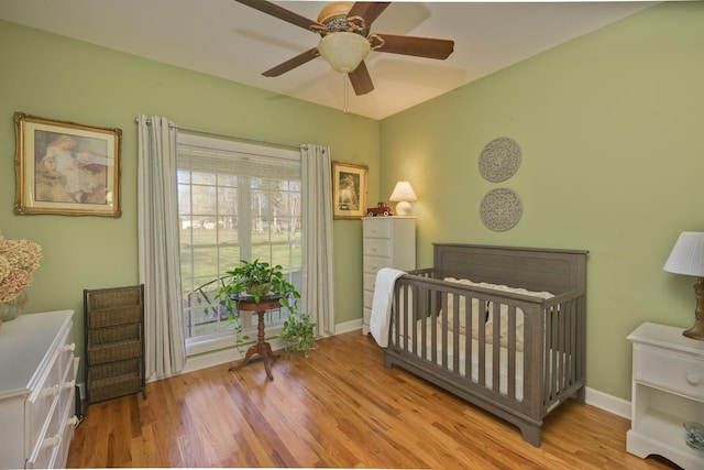 bedroom featuring a ceiling fan, a crib, baseboards, and wood finished floors