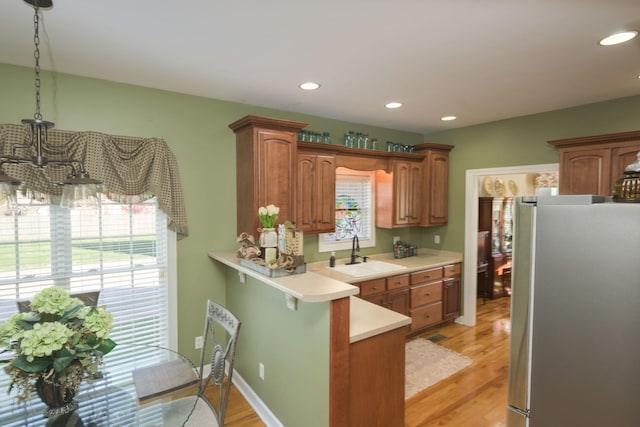 kitchen with light countertops, a sink, freestanding refrigerator, a peninsula, and light wood-style flooring