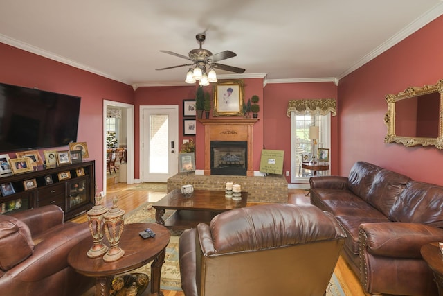 living area with crown molding, wood finished floors, a ceiling fan, and a brick fireplace