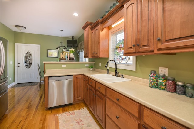 kitchen featuring light countertops, a sink, light wood finished floors, stainless steel dishwasher, and brown cabinets