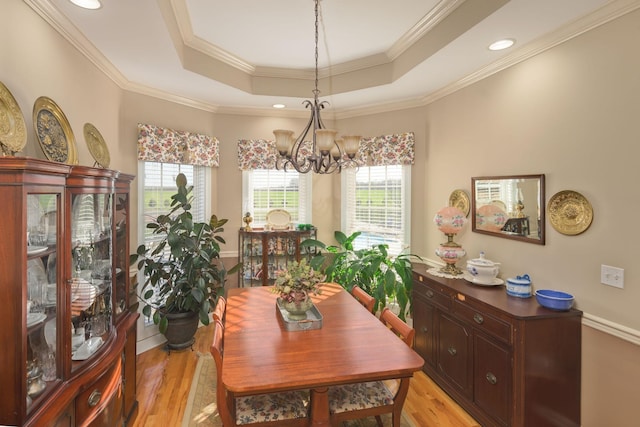 dining room featuring a tray ceiling, light wood-type flooring, ornamental molding, and an inviting chandelier