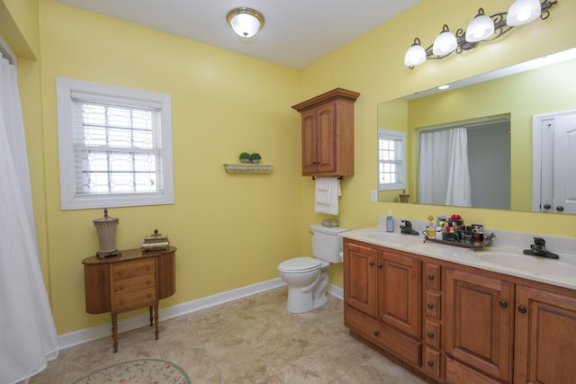 bathroom featuring baseboards, toilet, double vanity, and a sink