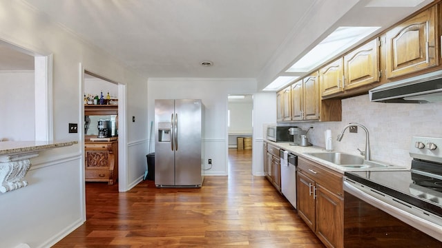 kitchen featuring ornamental molding, stainless steel appliances, backsplash, a sink, and wood finished floors