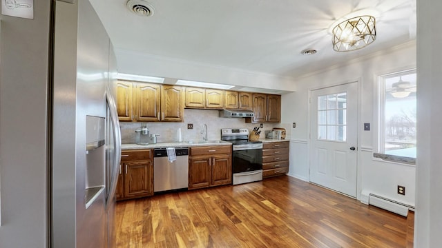 kitchen featuring a sink, appliances with stainless steel finishes, baseboard heating, under cabinet range hood, and ornamental molding