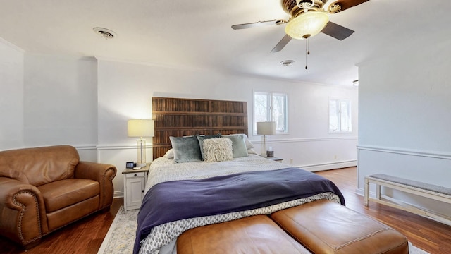 bedroom featuring ceiling fan, visible vents, baseboard heating, and wood finished floors