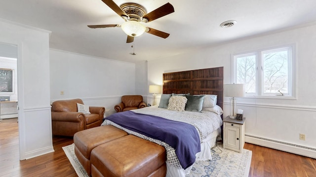 bedroom with a baseboard heating unit, ornamental molding, ceiling fan, visible vents, and wood finished floors