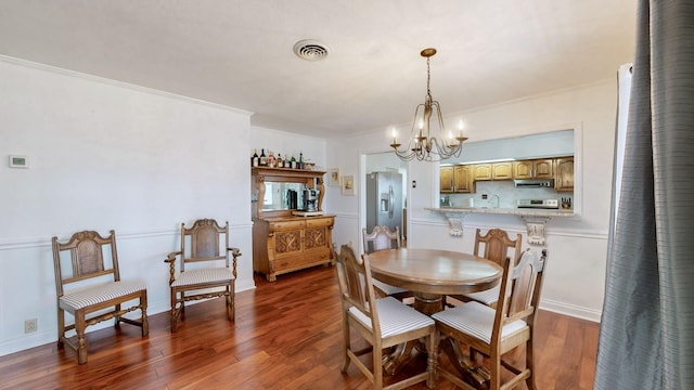 dining space with visible vents, wood finished floors, ornamental molding, and an inviting chandelier