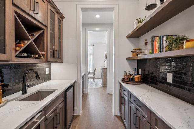 bar featuring light wood-style flooring, dishwasher, a bar, a sink, and backsplash