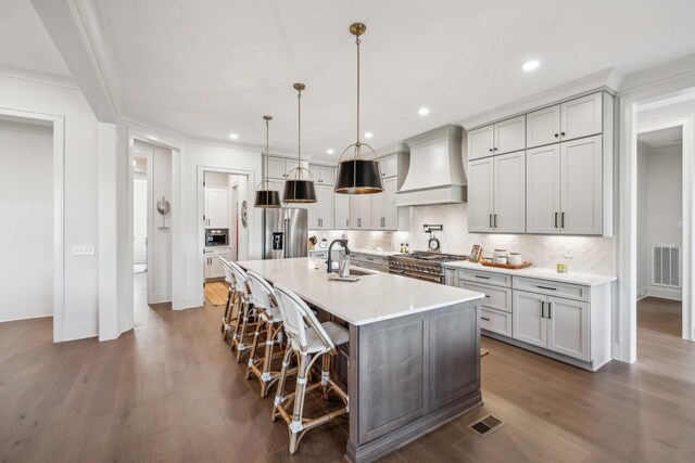 kitchen featuring a kitchen bar, appliances with stainless steel finishes, premium range hood, visible vents, and decorative backsplash