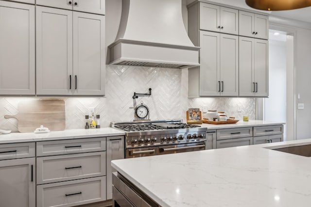 kitchen with gray cabinetry, range with two ovens, decorative backsplash, and premium range hood